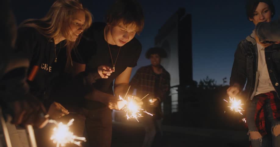 A small group of teenagers are outside lighting sparklers