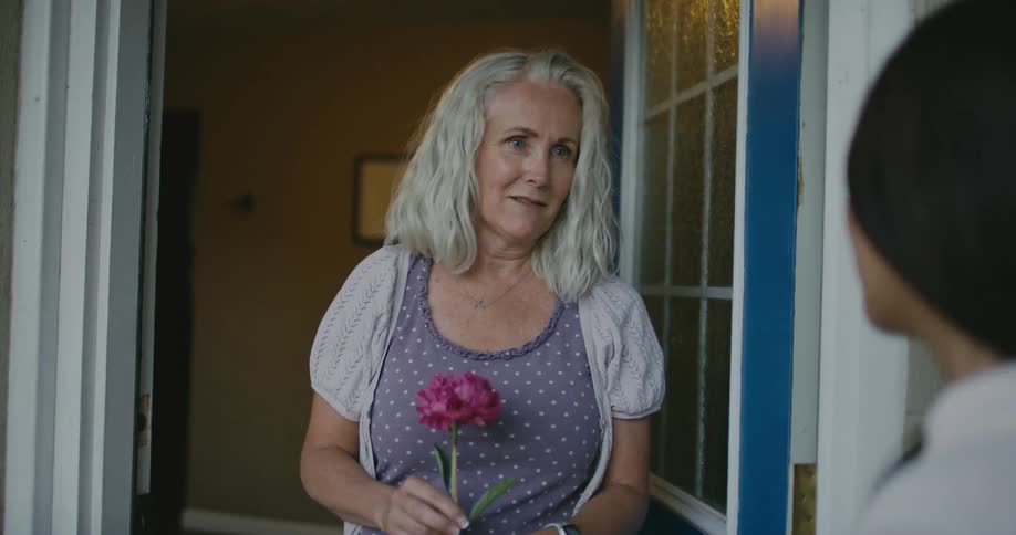 Older woman accepts flower from another woman with a smile and they stand and talk
