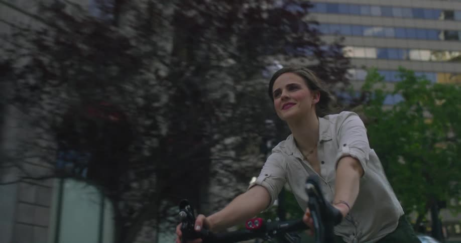 A girl is riding a bike past cars and buildings on a city street