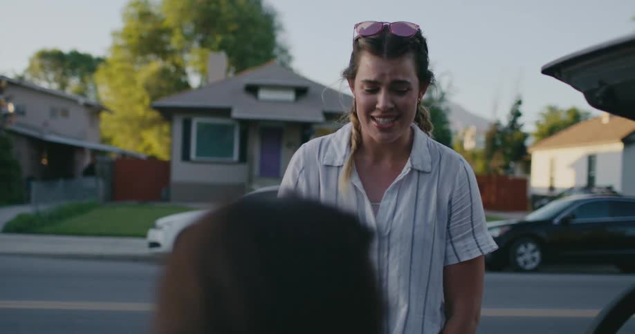 Woman with sunglasses and white shirt opens car boot in the neighborhood at sunset