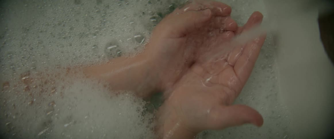 A child in a bubble bath has their hands under the running faucet