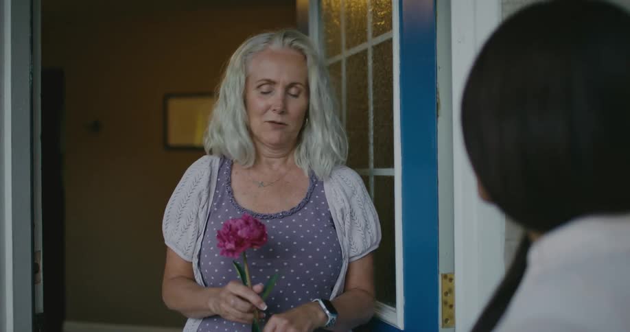 A woman brings a single rose to another womans door