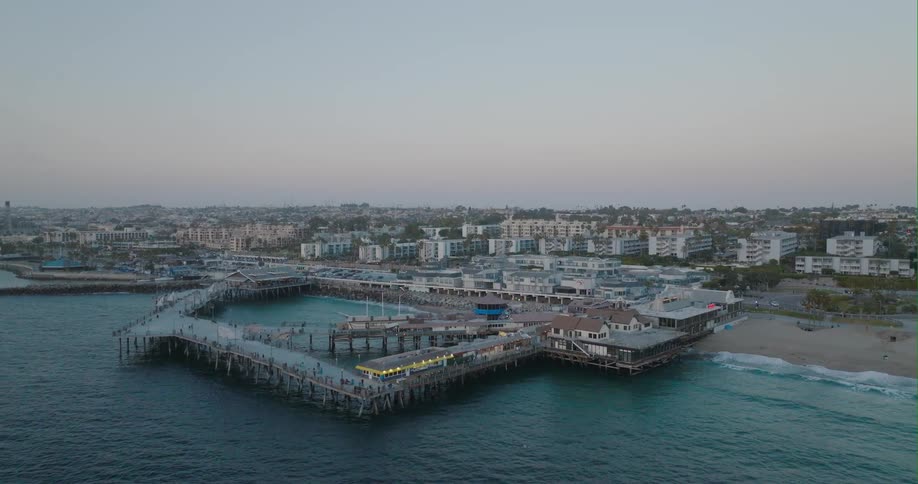 People wander around pier forming a closed shape near the beach with apartment buildings nearby