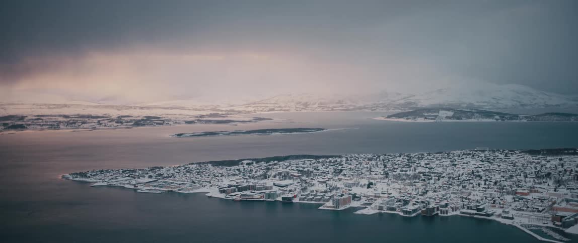 Sun brightens sky over snow covered lands across water from and equally snow covered town