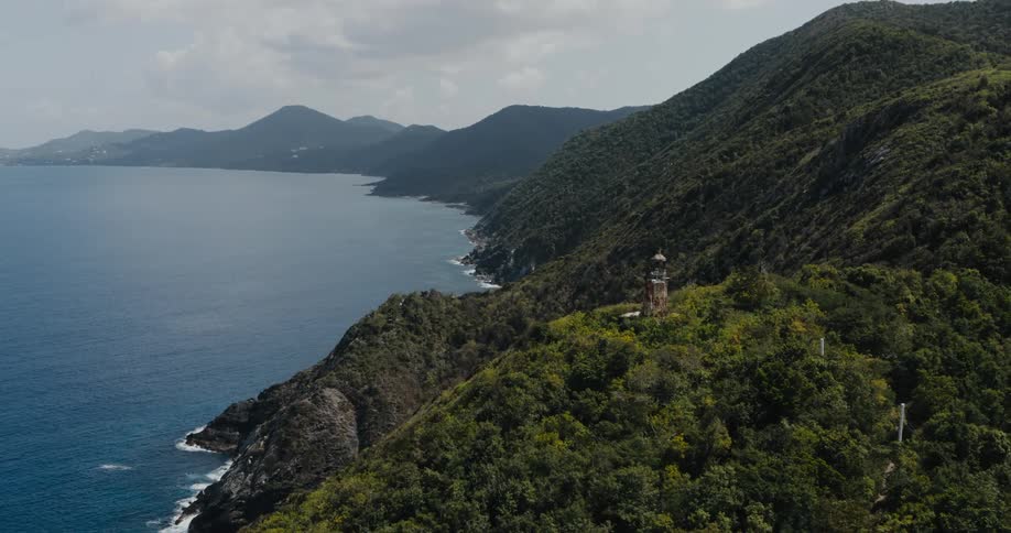 Poles lead to tower sitting on forest covered mountain overlooking the sea