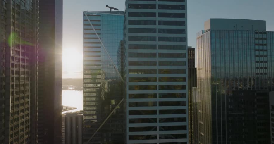 Dynamic orbit around tall skyscrapers as the sun peeks between buildings