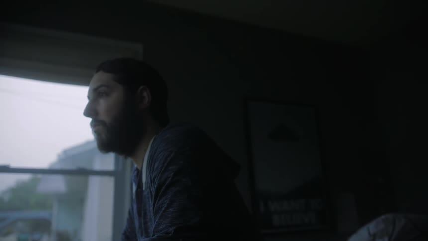 A man sitting on the edge of a bed as he stares off into the distance