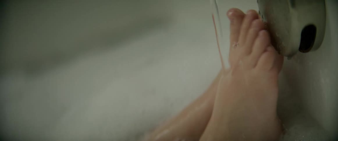 Child sitting in soapy bath puts feet under running water