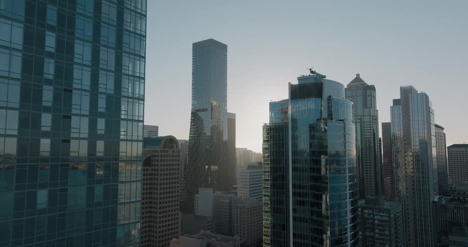 The rising sun glints through the glass and steel of tall skyscrapers and office towers