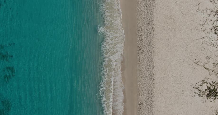 Aerial view of clear blue water waves rolling over a beach