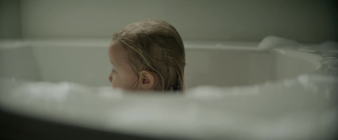 A little girl bathing in a bath tub throws a wash cloth in to the water