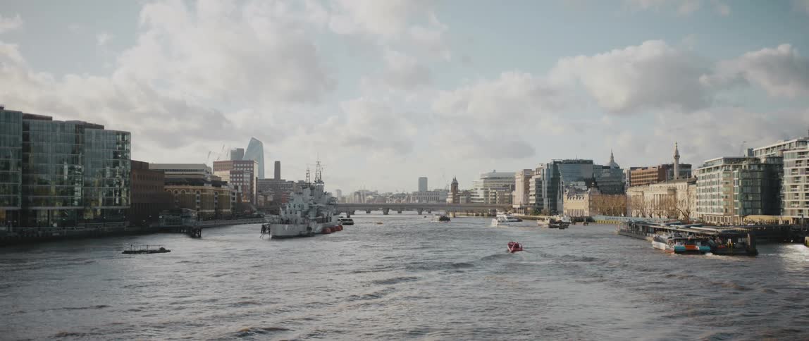 Boats are sailing on River Thames surrounded by buildings and tall downtown buildings can be seen in the distance