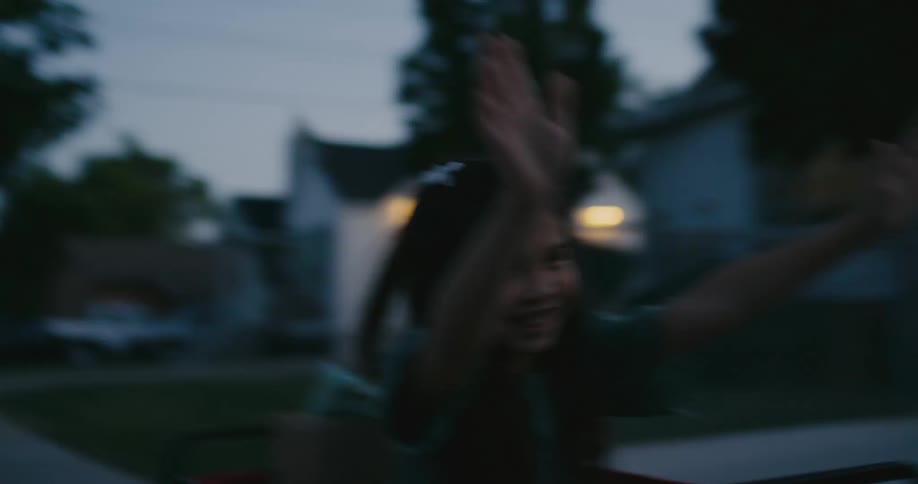 A young girl laughs while holding her arms up and riding down a sidewalk in a shopping cart