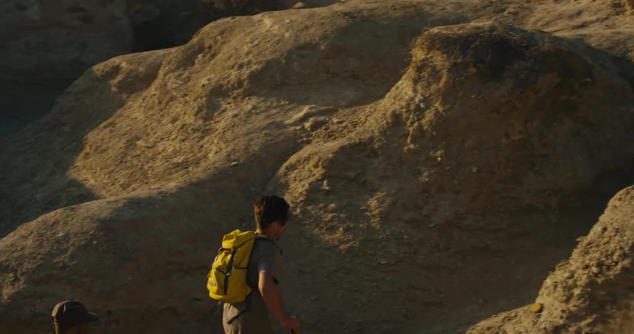 Two male hikers run up slope from gully in rough badlands
