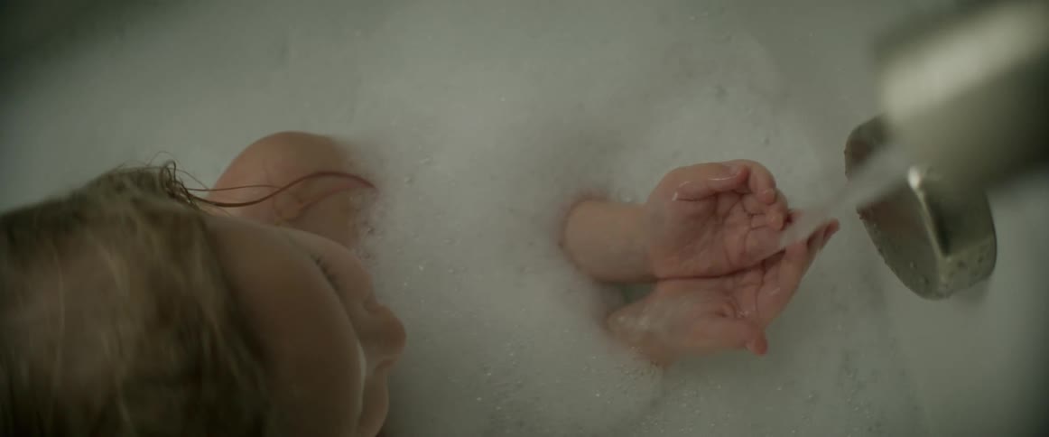 Child sitting in bubble bath holds hands in water streaming down from faucet