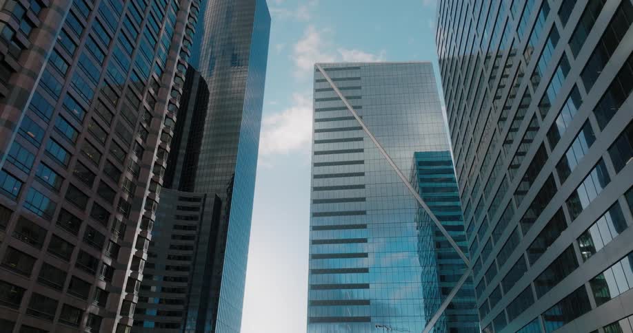 Push between tall downtown buildings as blue sky and clouds reflect from their surface