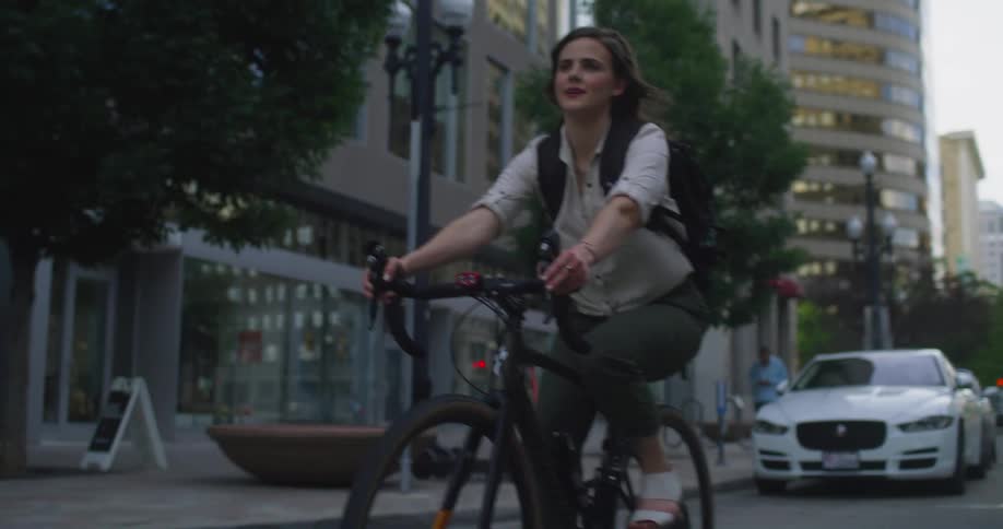 A woman rides her bicycle past vehicles downtown
