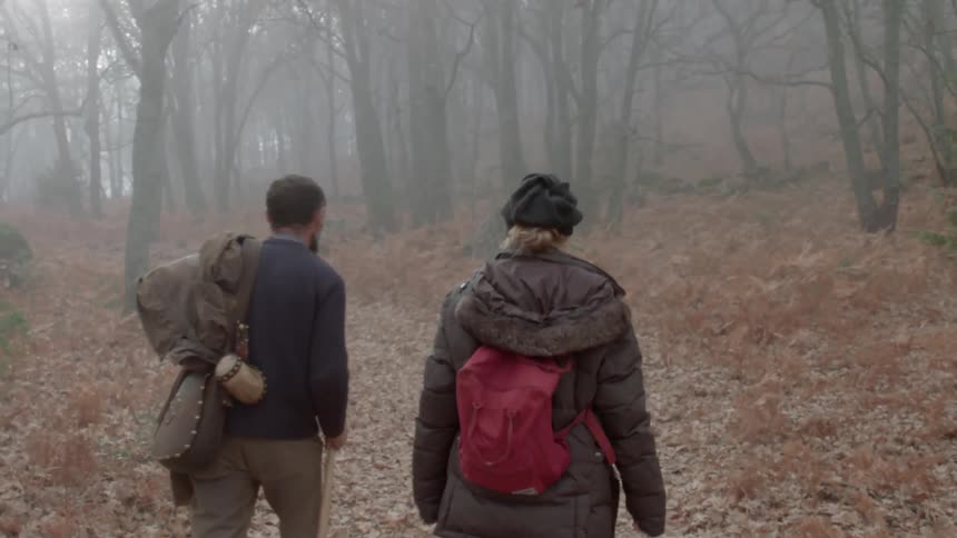 Male and female hikers hike through misty woods over dense layer of fallen leaves
