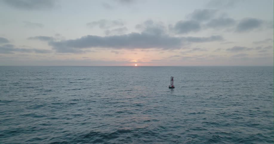 A buoy floats in the water as it ripples and waves and the sun is shining on the horizon