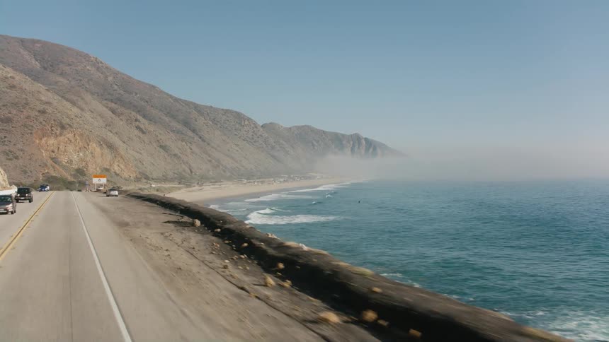 Vehicles travel an oceanside highway beside a mountain