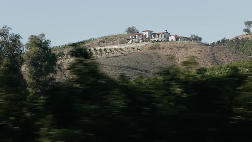A large home sits atop a hill overlooking crops on a farm