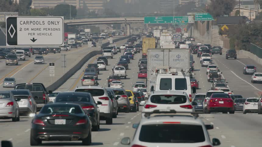 Dense traffic travels along a freeway through a city during the day
