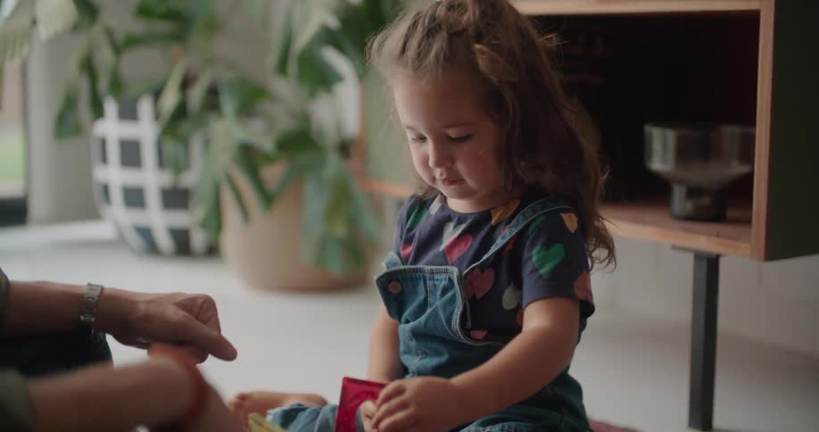 A man hands a building block to his daughter while playing together on the floor