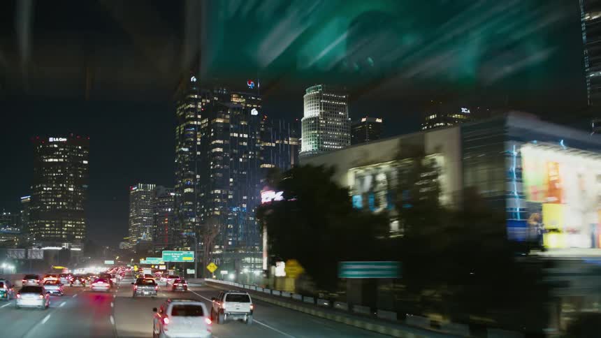 Heavy traffic on a highway traveling downtown at night with tall buildings and skyscrapers in the distance