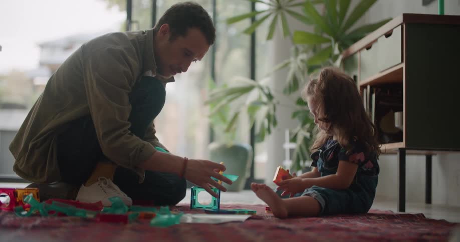A man is sitting on the floor with a little girl playing with toys