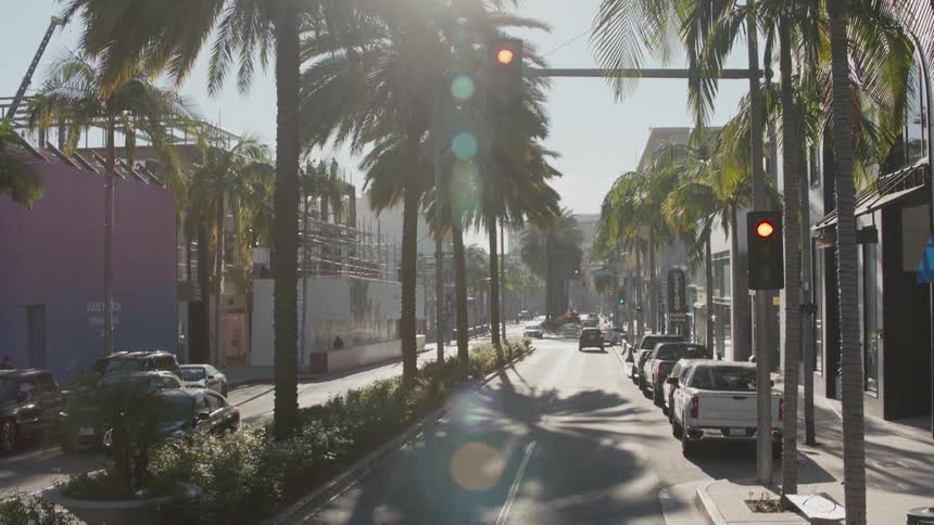 Traffic flows down street lined by palm trees and through intersection on a sunny day