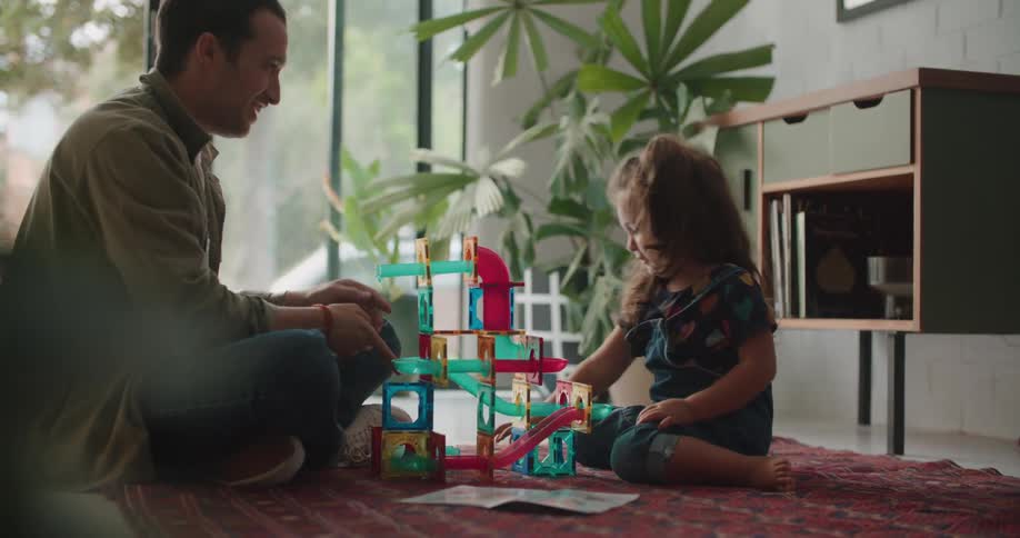 A man is sitting on the floor with a little girl playing with toys