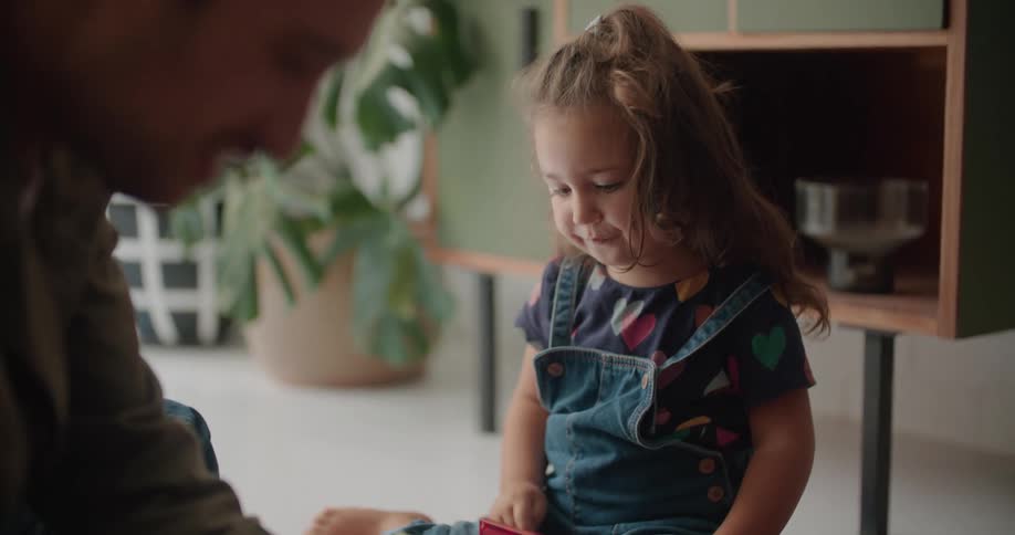 Father and daughter sit on a blanket with a lot of colorful square plastic toys and play with them