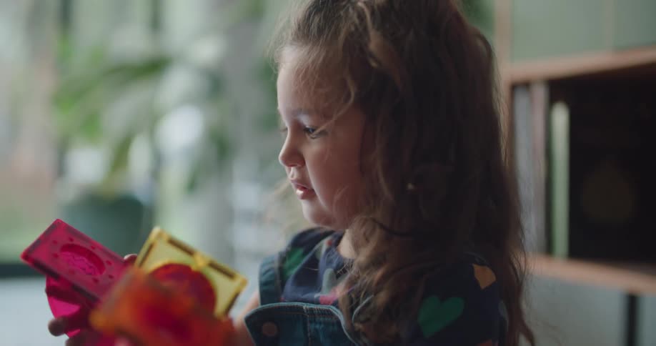 A little girl is holding a toy and turning it around and she hands it to someone