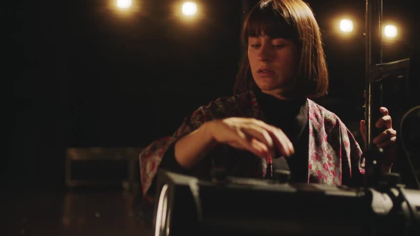 A woman is in a dark room turning knobs on a projector