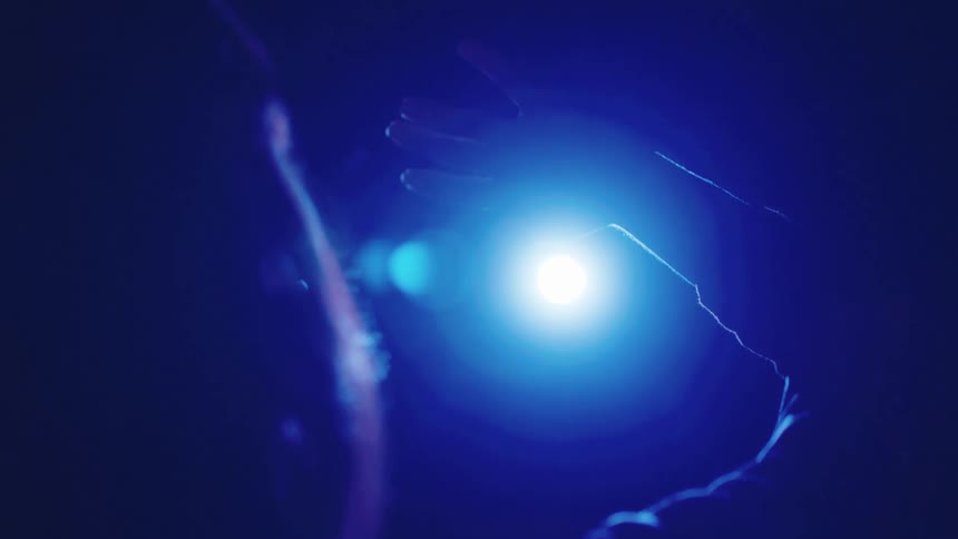 A woman is waving her hand in front of a bright light with a blue halo at night