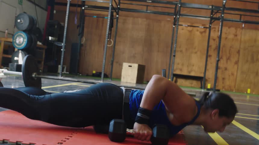 Woman with ponytail blue sport shirt and black leggings works out with dumbells in the gym