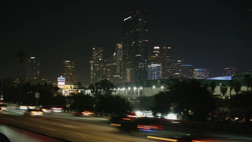 Heavy traffic on a highway traveling downtown at night with tall buildings and skyscrapers in the distance