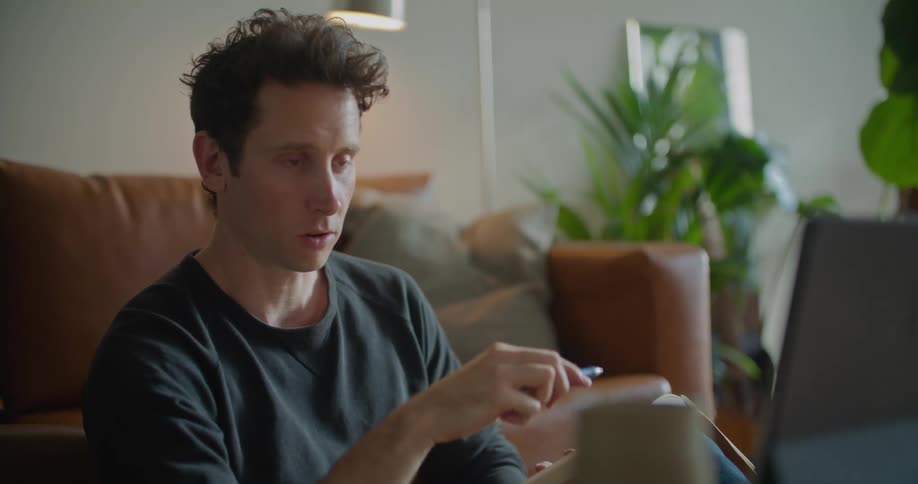 Man sits on the floor in his living room gesturing and talking during a video conference