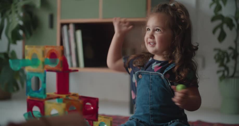 Daughter with curly hair and mother sit on floor playing with toys in the living room