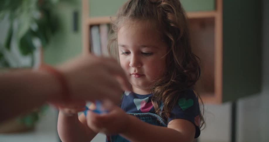 Girl with curly hair and mother sit on the red rug playing with toys
