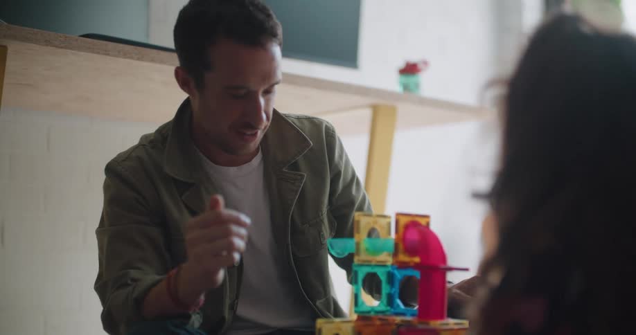 A man plays with toys with a young girl while sitting on the floor indoors during the day