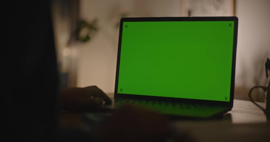 A person sitting in front of a laptop computer is tapping their fingers as they look at a green screen