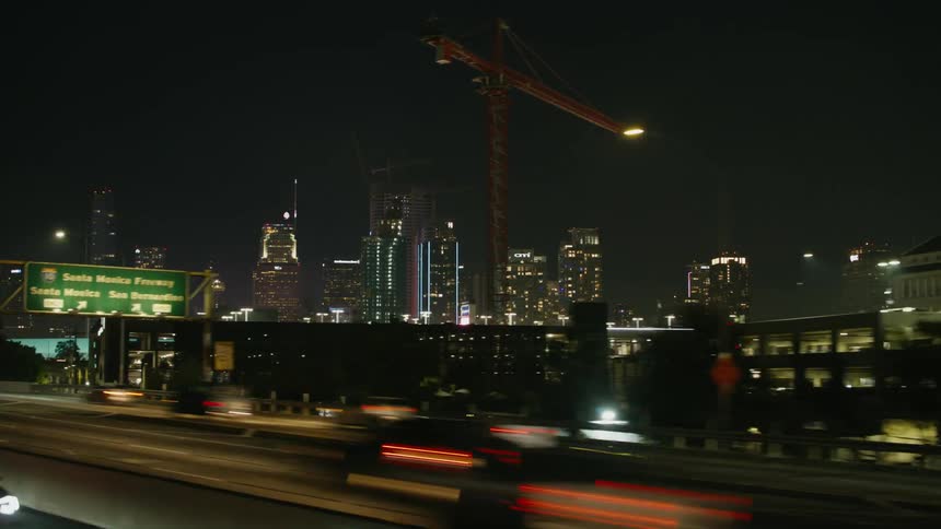 Time lapse of vehicles driving on a freeway in a city past construction cranes and office buildings