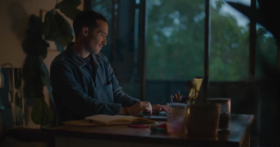 A man sits in his office and smiles as he looks at his computer and some pieces of plastic