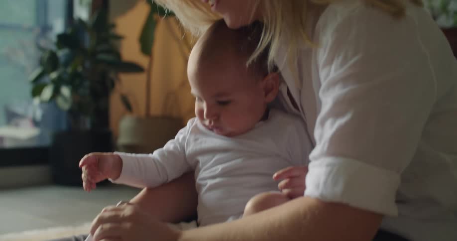 A woman sitting on the floor puts a sock on the foot of a baby resting in her lap