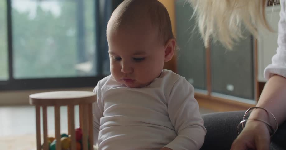 Blonde mother with white shirt and bracelets sits on the floor playing with toys together