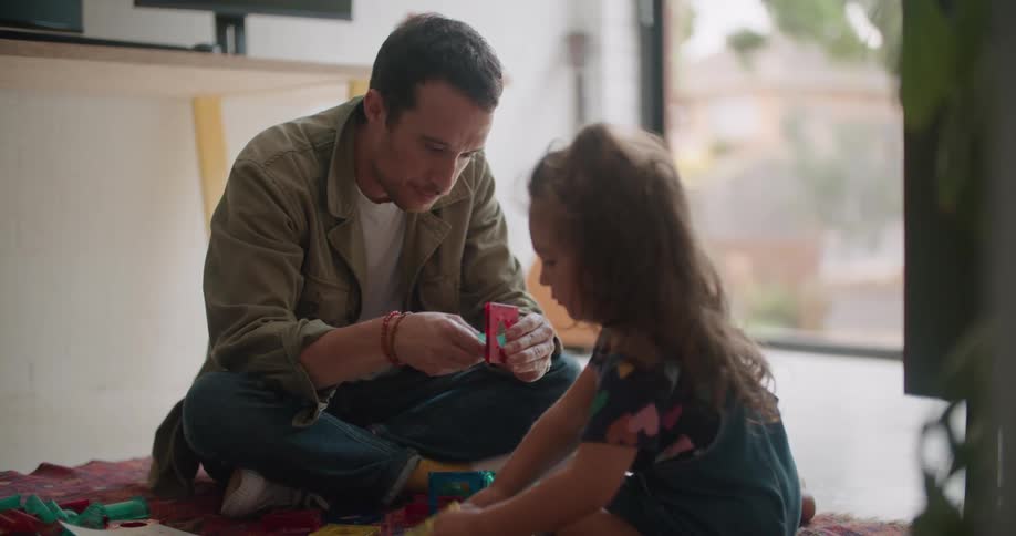 Father sitting on the carpet in the floor playing with some toys with his daughter