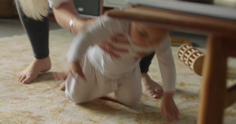 A woman at home chases after her baby that crawls away and then picks her up and points at something