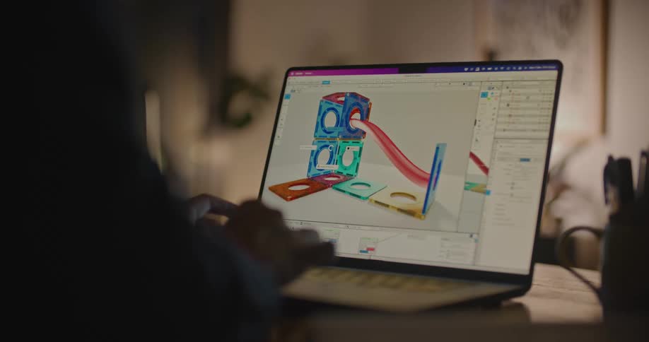 Designer working on a 3d model of a toy on a laptop at night