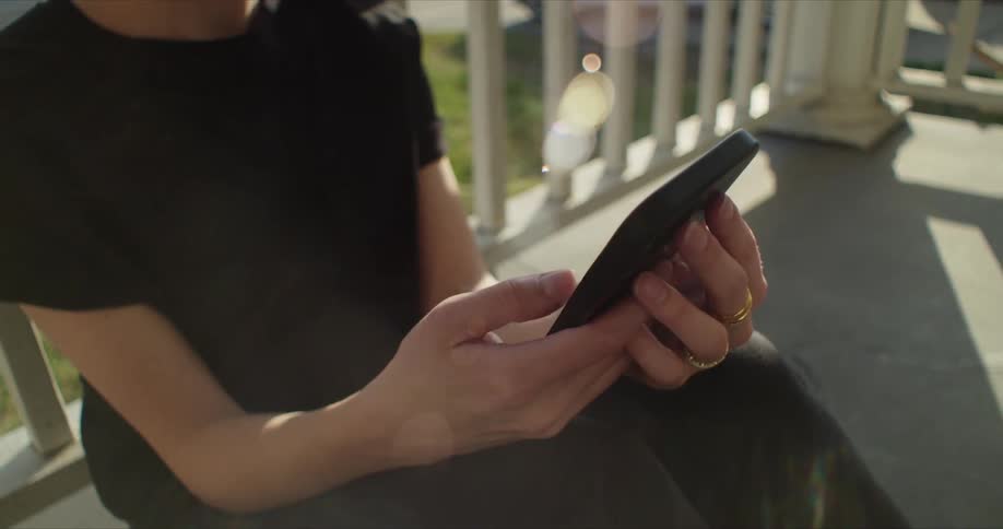 A woman is sitting outside on the front porch of a house using her phone